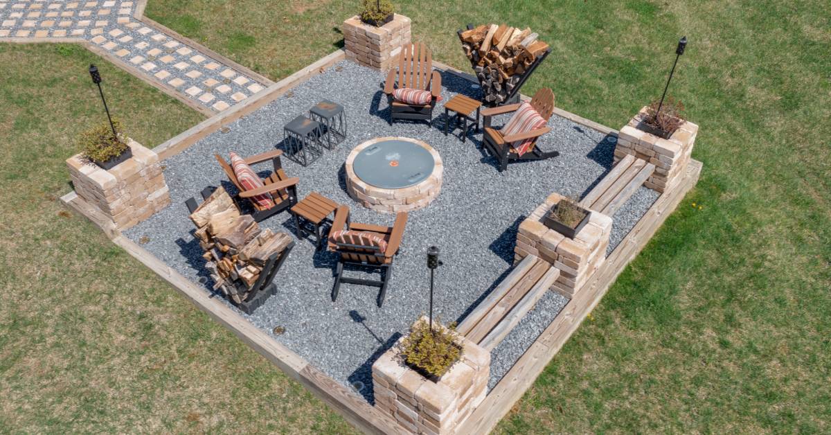 A large gravel-filled patio that has a firepit and plenty of seating available. There is a path the leads back to the house.