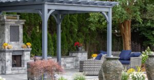 A vibrant backyard patio with a fireplace, tons of seating, and a pergola. There's also a line of trees in the background.