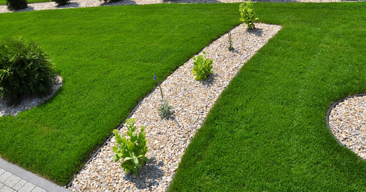 A freshly cut section of grass that has sections of bushes and trees surrounded by rocks.