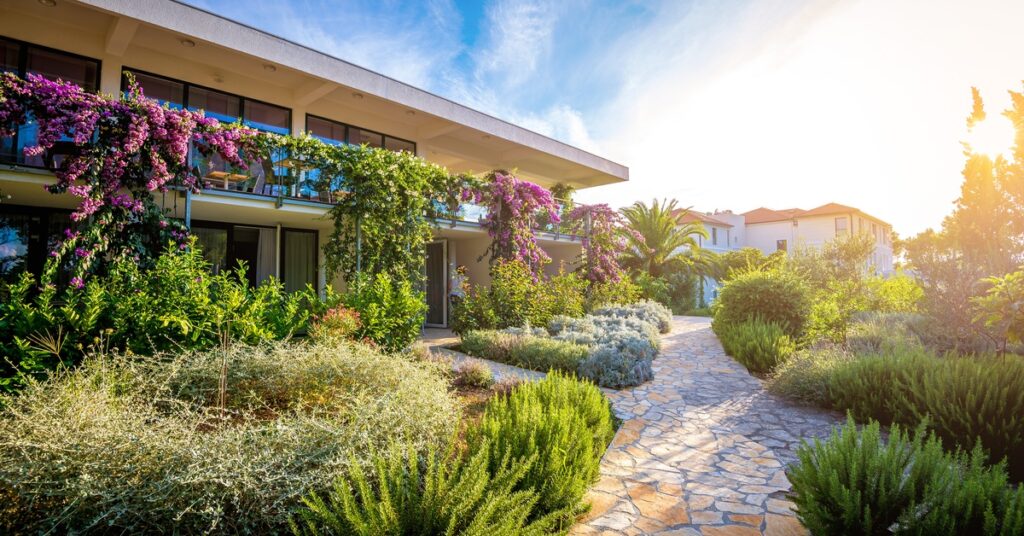 A vibrant garden with colorful plants hanging from the building. A stone pathway cuts through the middle of it.