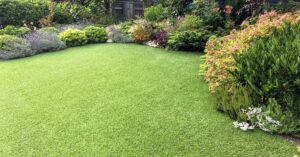 A lush backyard with a perfectly maintained artificial lawn, surrounded by flowering bushes and shrubs.