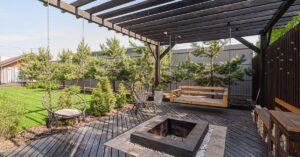 An in-ground fire pit surrounded by pebbles and concrete sits in the middle of a black wooden deck.