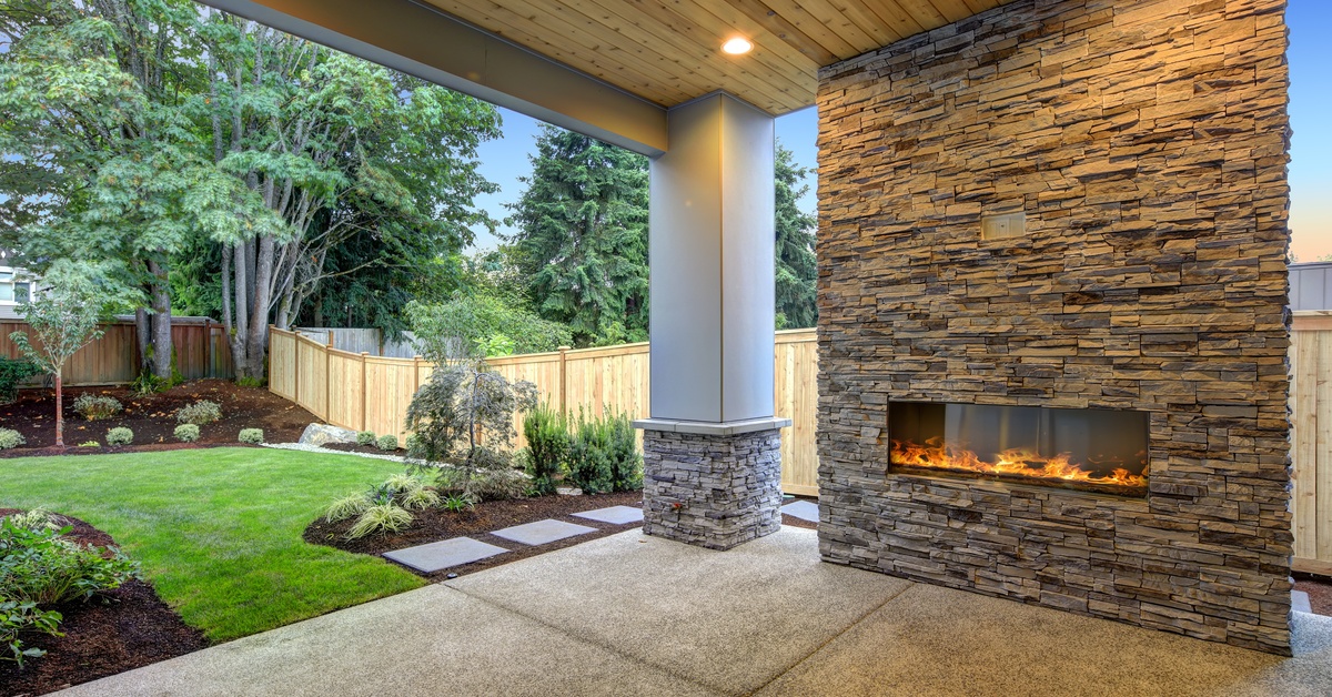 A beautiful, modern outside patio contains a large fireplace, a concrete floor, and a large pillar.