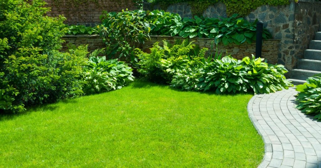 A well-landscaped yard features bright green grass, several green plants, and a gray brick pathway.