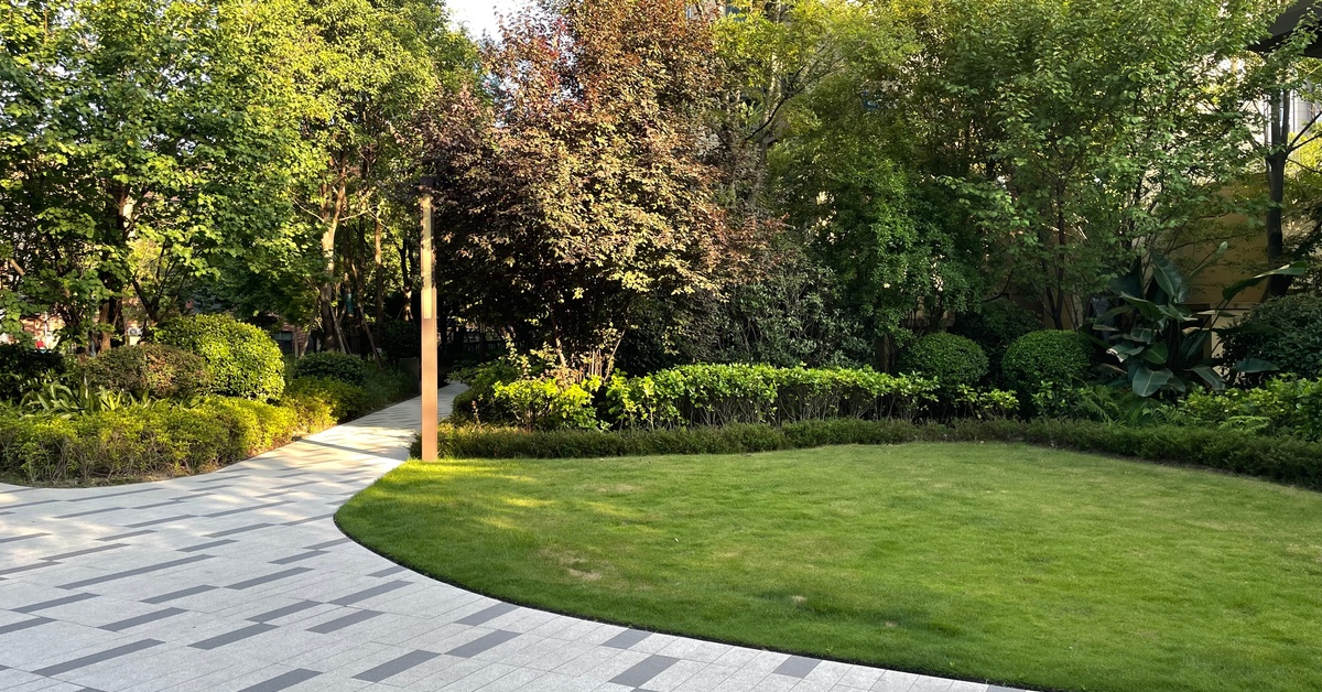 A beautifully landscaped commercial property features a gray brick walkway, green grass, trees, and bushes.