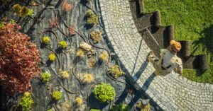 An aerial view shows a professional landscaper standing on a pathway smoothing out dirt to apply rolls of sod.