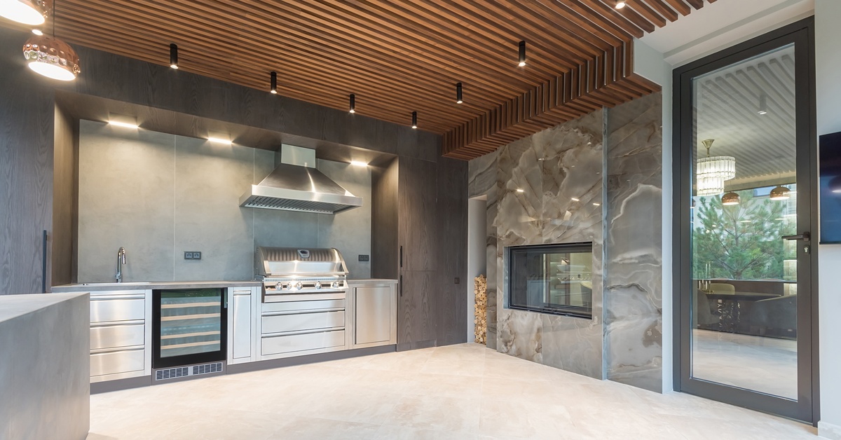 A luxurious modern outdoor kitchen features a large grill, wine cooler, fireplace, and metal cabinets.
