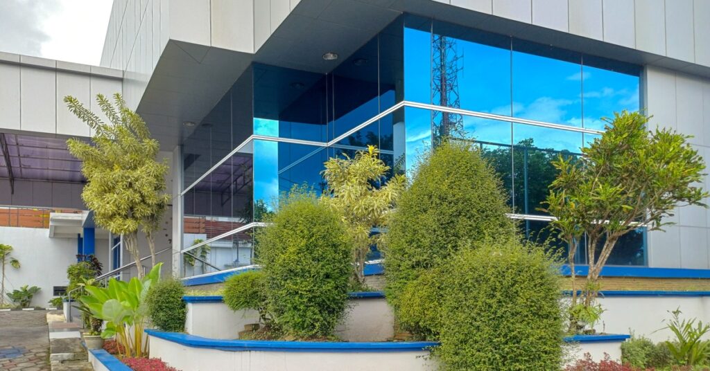 The outside of a commercial building features large windows and layers of retaining walls with manicured trees and bushes.