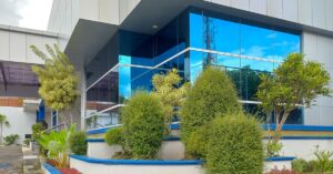 The outside of a commercial building features large windows and layers of retaining walls with manicured trees and bushes.