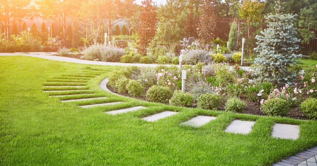 A beautifully landscaped residential backyard features several paved walkways around flower beds.