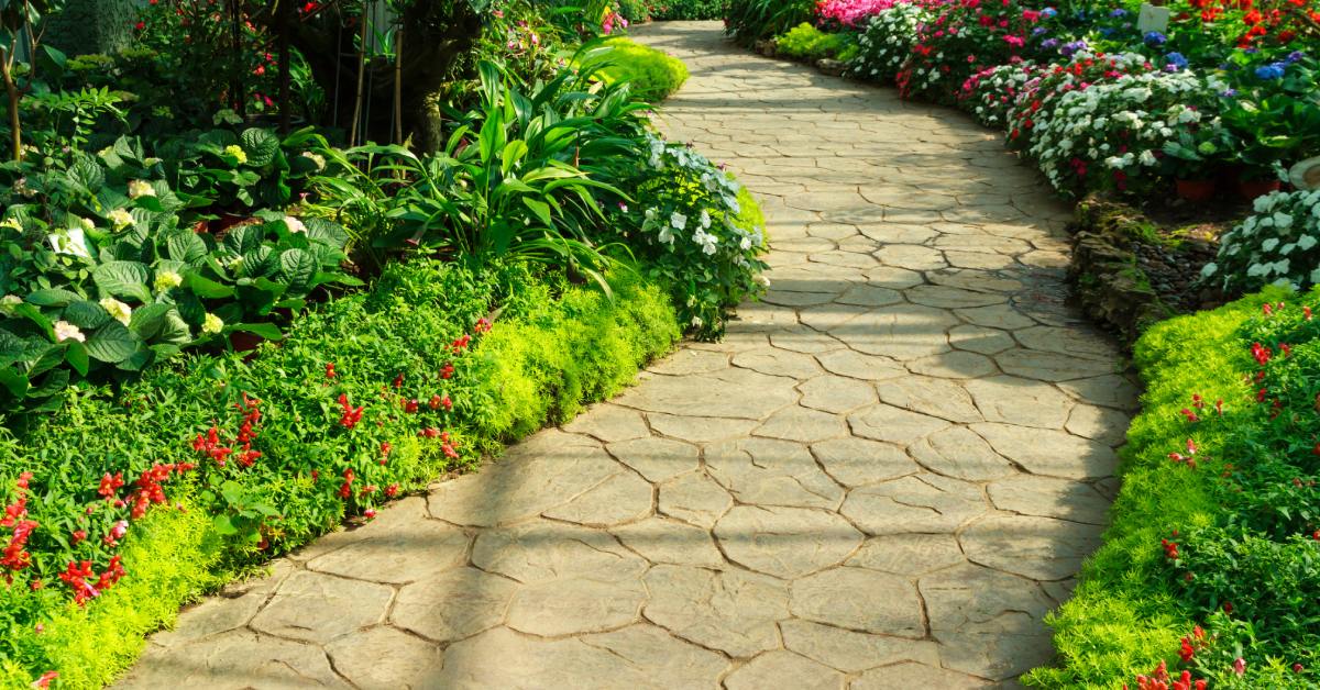 A beautiful stone walkway is lined with pink, red, white, and blue flowers. There's also a lot of greenery.