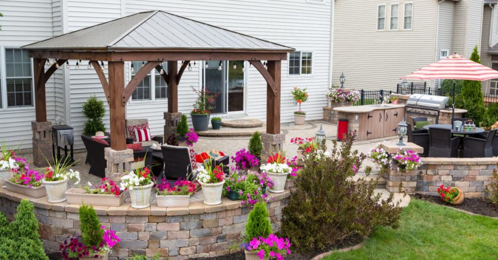 A residential backyard features a brick patio with a brick wall surrounding it, patio furniture, and potted plants.