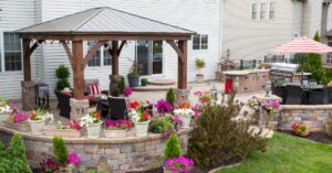 A residential backyard features a brick patio with a brick wall surrounding it, patio furniture, and potted plants.