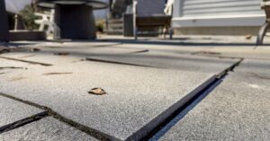 A close-up view shows a concrete patio beginning to crack and become raised. A table and chairs are in the background.
